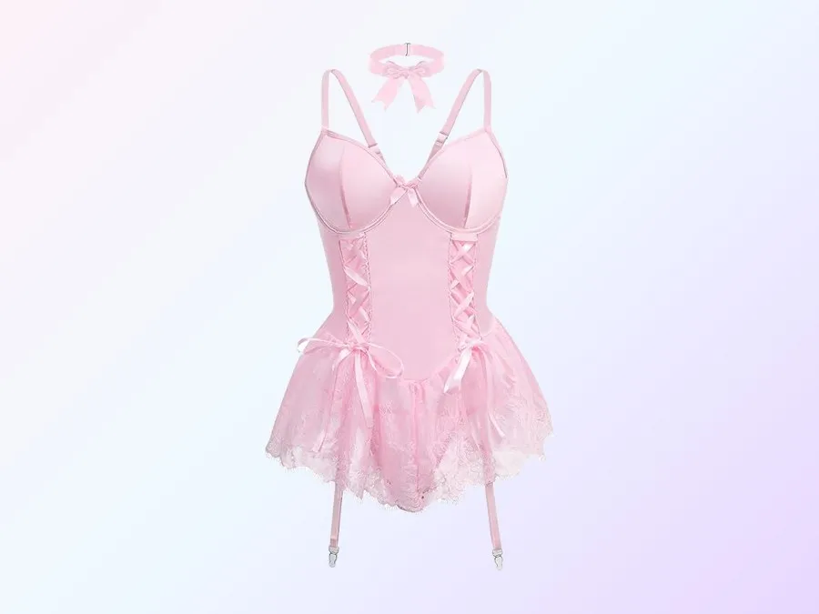 A baby pink babydoll laid flat, underwire cups, satin lacing and little bows down the front, a skirt of pale pink lace and short garter straps, a matching pink choker tied in a bow above it, on a soft pink and lavender gradient.